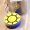 Dose mit aufgeklebter Sonnenscheibe vor einem Kochtopf